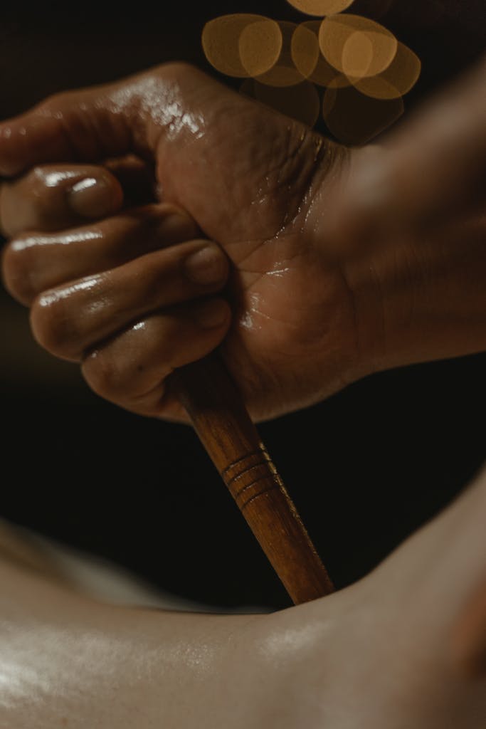 A close-up of a hand holding a wooden massage tool, set against a dark background.
