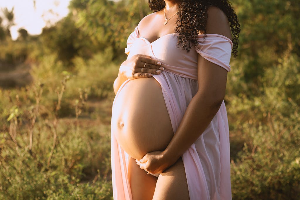 Pregnant woman in pink dress posing outdoors during a summer maternity photoshoot.